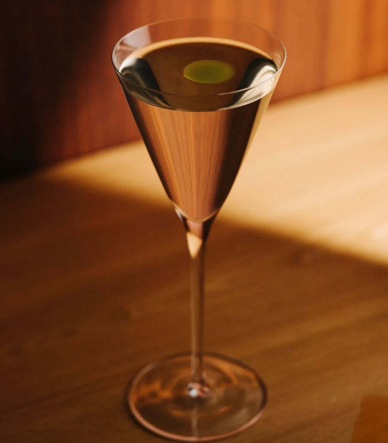 A stemmed cocktail with a green garnish in warm amber light
